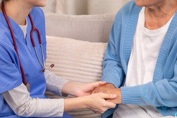Obraz premium Young female nurse holding hands with senior woman, both smiling with trust and warmth during health support session in cozy home setting, healthcare, caregiver, take care, consult.