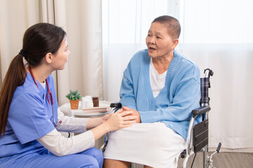 Senior woman in wheelchair discussing health with nurse on sofa, both smiling and sharing emotional...
