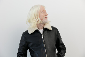 Man with long white hair in a black leather jacket looking upwards against a minimalistic light...