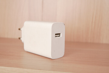 Minimalist photograph of a white USB wall charger on a wooden surface suitable for tech blogs or...