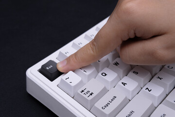 Modern close-up photograph of a finger pressing the Esc key on a white keyboard for tech visuals or...