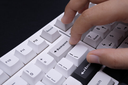 Modern minimalist close-up photograph of finger on backspace key white keyboard for tech visuals editing concepts and digital interface design