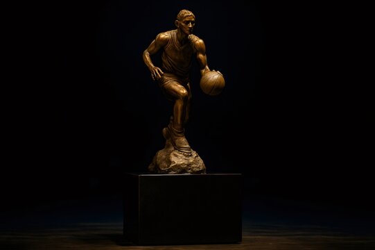 Bronze statue of basketball player dribbling with ball on dark background