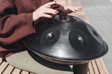 young caucasian woman playing black handpan with hands, ethnic metal drum instrument, sits on...