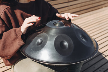young caucasian woman playing black handpan with hands, ethnic metal drum instrument, sits on...