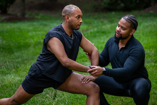 A personal trainer helping a client with a yoga pose outdoors