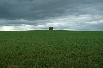 Green field with an old windmill and stormy clouds