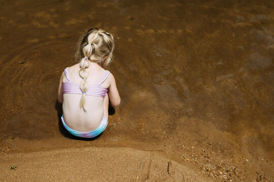 Young girl kneeling on sandy riverbank playing quietly in water