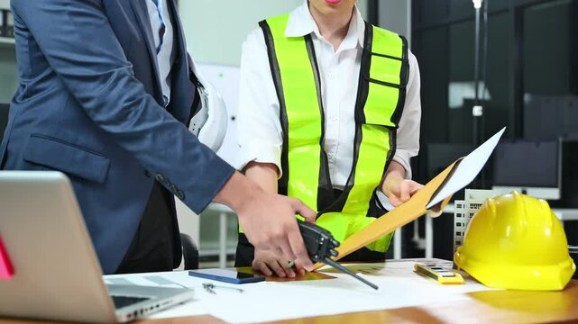 Construction manager and engineer discuss floor plan and project safety with tablet and blueprints