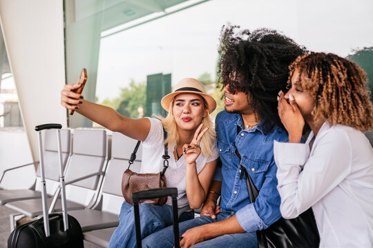 Multiracial group of friends taking a selfie with a smartphone while waiting for their flight at the airport