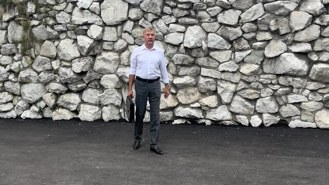 man, walking, stone wall, casual, outdoor, sunny day, stylish attire, urban, nature, relaxation, leisure, scenery, pavement, stroll, daytime, sunlight, gray stones, relaxed atmosphere, solitary, actio