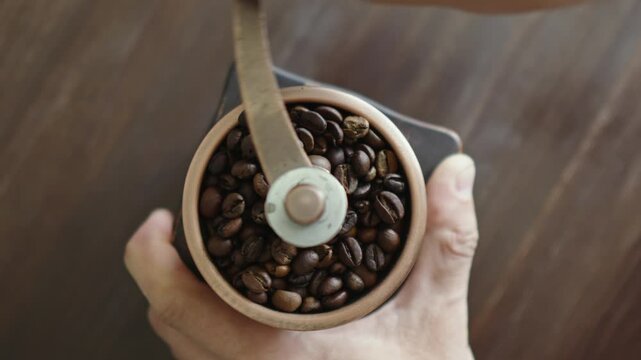 Grinding of aromatic coffee beans with a manual coffee grinder. Smooth rotation of the camera. Top view