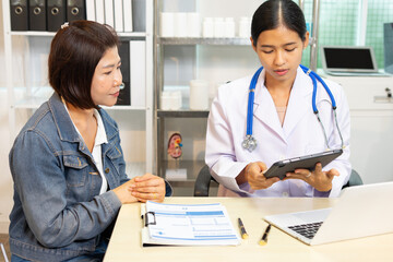 Female doctor consulting patient with medical documents and laptop in clinic