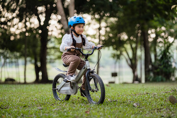 A young girl is riding a bike in a park. She is wearing a helmet. The bike is silver and has a black seat