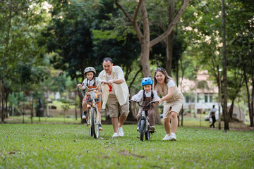 A family of four riding bikes in a park. A man is riding a bike with a child on it