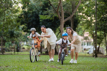 A family of four riding bikes in a park. A man is riding a bike with a child on it