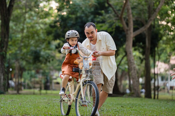 A man is helping a child ride a bike. The child is wearing a helmet. The bike is parked in a grassy...