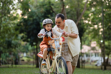 A man is helping a child ride a bike. The child is wearing a helmet. The bike is a tricycle