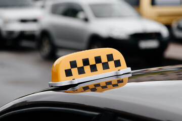 taxi sign, black checkers on yellow background, closeup view, sity street with cars in background