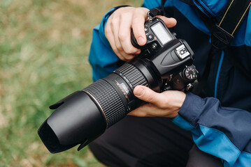 black dslr camera in hands, large long lens, young caucasian man photographer at work outdoors in...