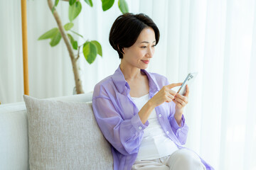 部屋でスマホを操作するミドル女性