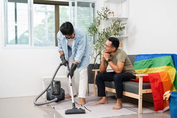 Teamwork in Cleaning. Two friends organizing their living area with a rainbow flag in the background.