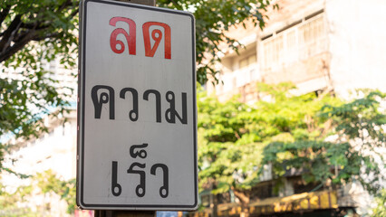 Thai speed-reduction warning sign with red lettering on a city roadside