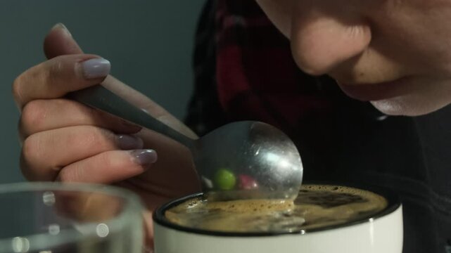 Barista carefully stirs coffee in circular movements using teaspoon. Female taster in shirt sniffs drink before tasting cup of espresso