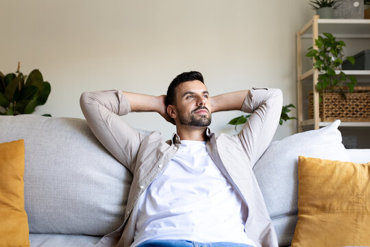 Happy adult man relaxing on the couch with hands behind the head looking away feeling satisfied.