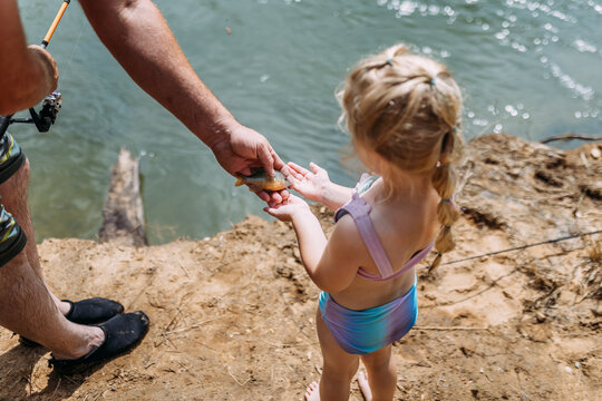 Dad showing sunfish to young daughter on riverbank