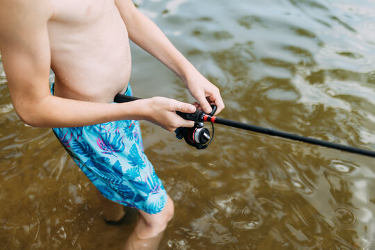 Close up of child wading in river reeling fishing pole