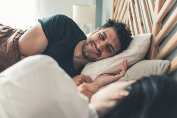 Male and female bonding relationship, Couple lying on bed smiling and holding hands, woman looking...