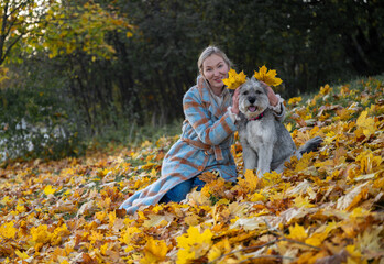 Smiling woman in coat with her mixed-breed dog enjoying autumn leaves in a park
