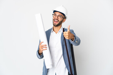 Young architect man with helmet and holding blueprints isolated on white background with thumbs up...