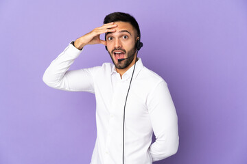 Telemarketer man working with a headset isolated on purple background doing surprise gesture while looking to the side