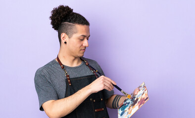 Young artist man holding a palette over isolated purple background