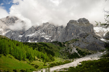 Dramatic Dachstein mountain peaks with lush green valley and clouds in Austria