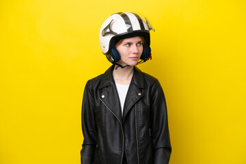Young English woman with a motorcycle helmet isolated on yellow background looking to the side