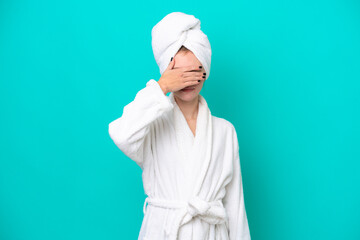 Young woman in a bathrobe isolated on blue background covering eyes by hands. Do not want to see...