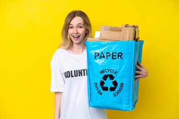 Blonde English young girl holding a recycling bag full of paper to recycle isolated on yellow...