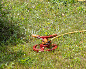A red sprinkler is on the grass