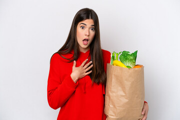 Young Brazilian woman holding a grocery shopping bag isolated on white background surprised and...