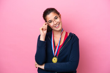 Young Brazilian sport woman with medals isolated on pink background with glasses and happy