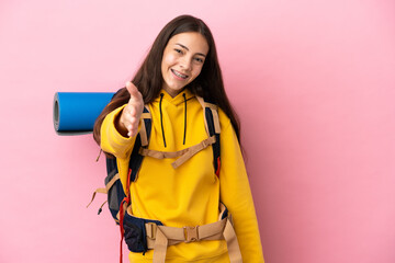 Young mountaineer girl with a big backpack isolated on pink background shaking hands for closing a...