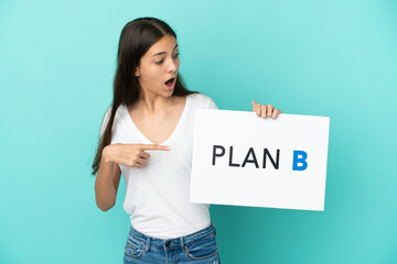 Young French woman isolated on blue background holding a placard with the message PLAN B with...