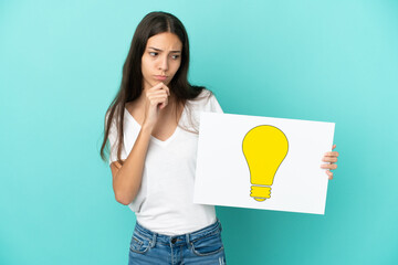 Young French woman isolated on blue background holding a placard with bulb icon and thinking
