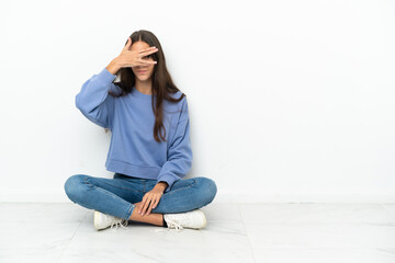 Young French girl sitting on the floor covering eyes by hands and smiling
