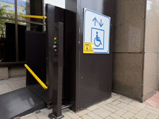 Vertical platform lift for wheelchair users installed outside building entrance with accessibility...