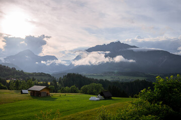 Peaceful alpine valley with wooden barns, green meadows and misty mountains at sunset in Austria