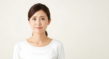 Portrait of a Concerned Asian Woman in White, Soft Lighting, Neutral Background.